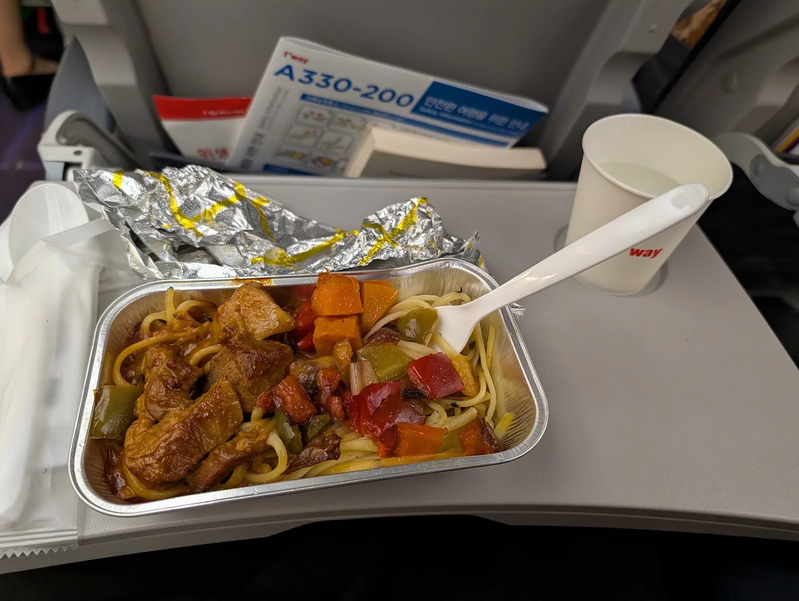 La cena servida a bordo: pasta con pollo y verduras en bandeja de aluminio
